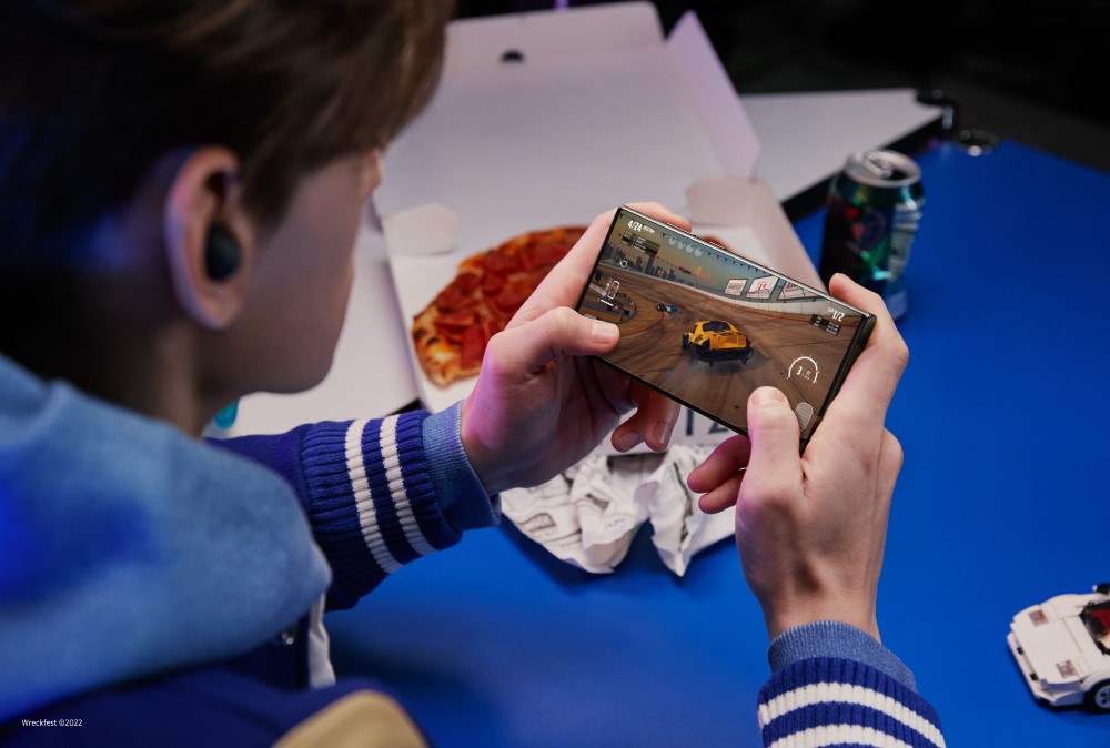 Un adolescent tient entre ses mains le Samsung Galaxy S23 Ultra et joue à un jeu vidéo de course automobile.