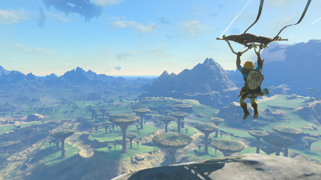 Link vole accroché à un deltaplane dans le ciel au-dessus d'un vaste paysage de plaines et de montagnes.