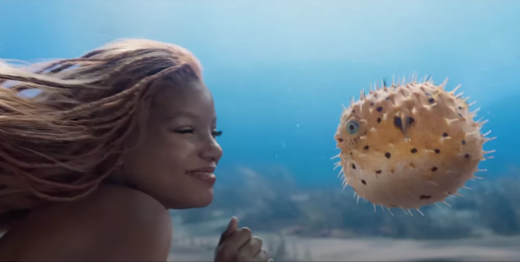 Image du film La Petite Sirène de Disney, Halle Bailey sous l'eau dans le rôle d'Ariel qui s'approche d'un poisson.